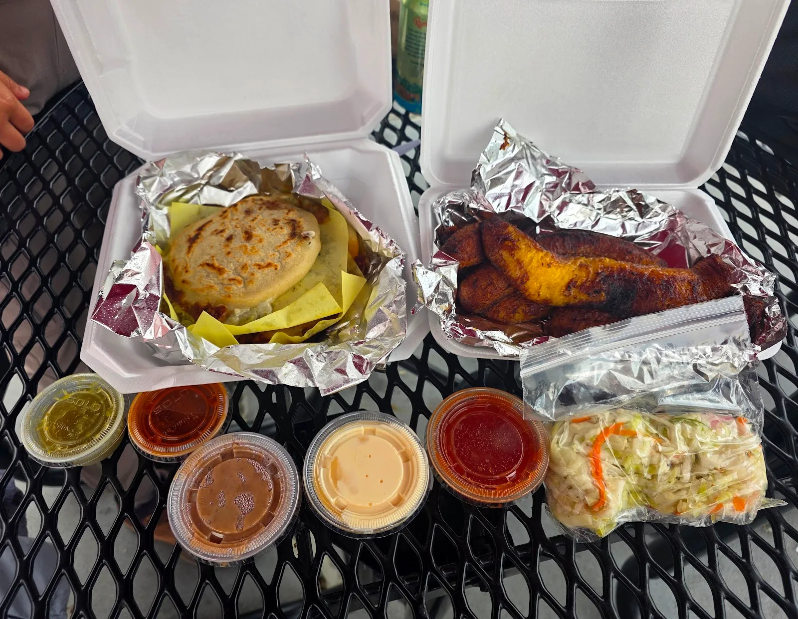 Takeout spread of pupusas, fried plantains, curtido and a row of house salsas